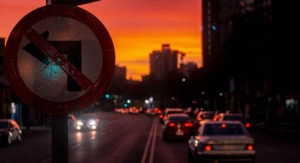 Placa de transito em Santiago, proibindo virar a esquerda e ao fundo vários carros no final do dia. Representa aluguel de carro em Santiago.