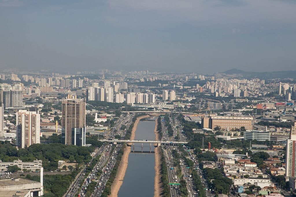 Imagem de cima da capital paulista. O rio Tietê no meio e ao redor vários prédios e carros.
