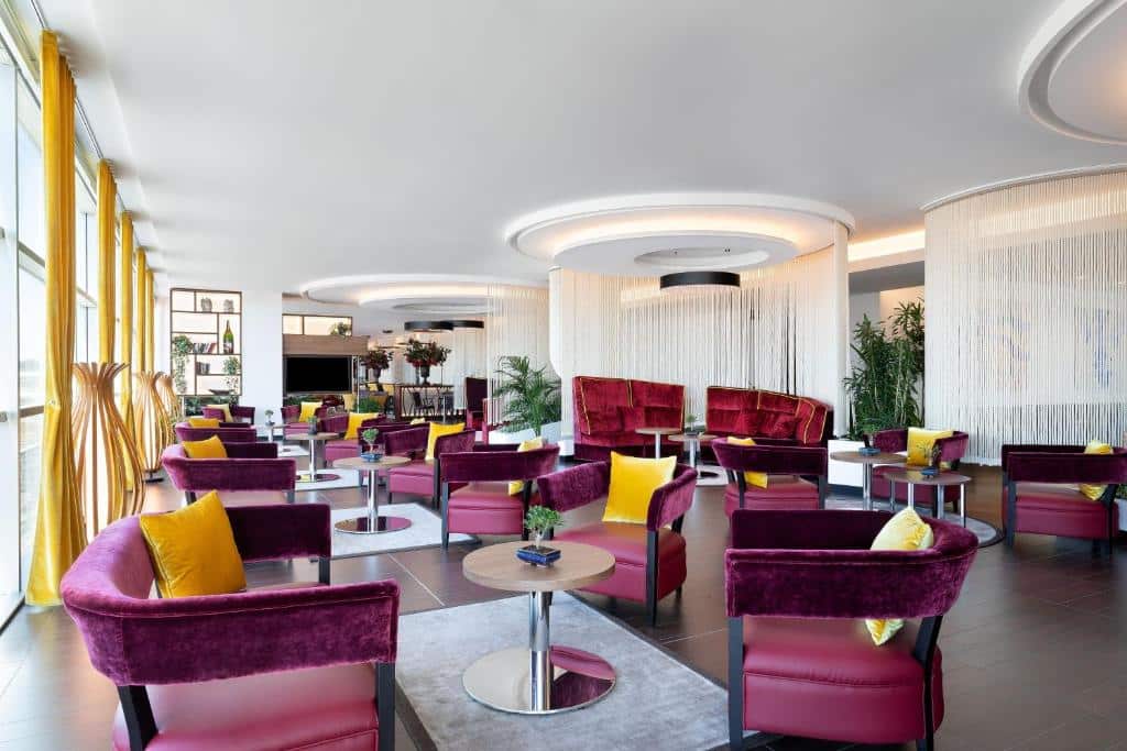 Área de convivência do Sheraton Milan Malpensa Airport Hotel & Conference Centre com diversas poltronas estofadas na cor vinho com almofadas douradas, o local passa um certo ar de requinte