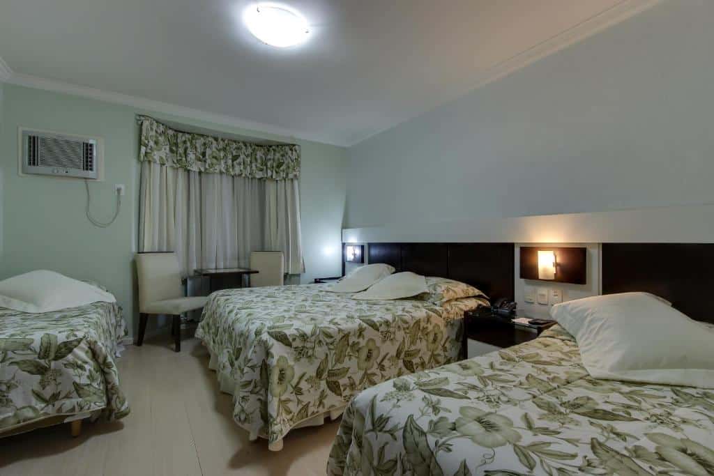 suíte quadrupla do hotel glamour da serra com três camas, uma de casal e duas de solteiro, com jogos de lençóis estampados combinando com as cortinas.
