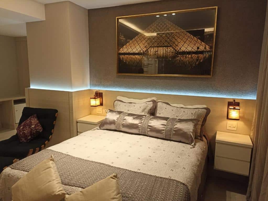 Quarto de hotel com uma cama de casal com uma luz de led na cabeceira e quadro do museu do louvre em cima. Imagem para ilustrar o post hotéis em Cabo Frio.