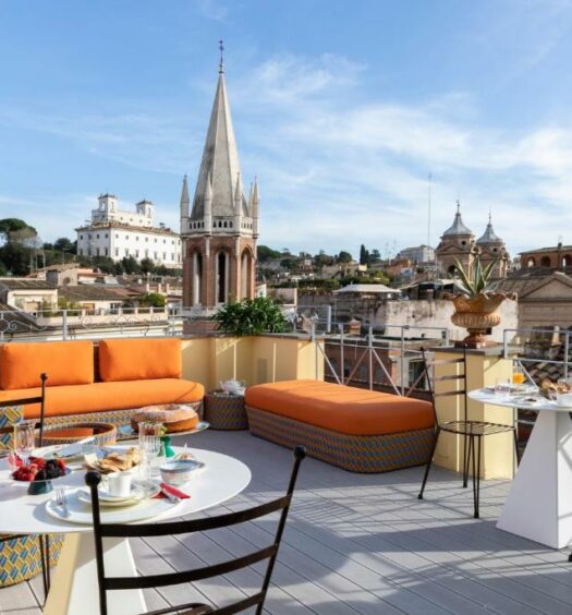 terraço com vista da cidade no Poēsis Experience Hotel, um dos hotéis boutique em Roma, com cadeiras de ferro, mesinhas redondas, sofás amarelos e um café da manhã servido em cima delas