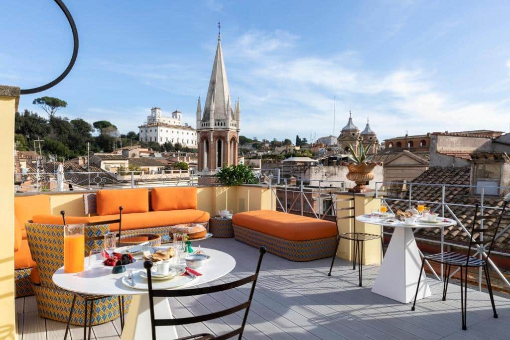 terraço com vista da cidade no Poēsis Experience Hotel, um dos hotéis boutique em Roma, com cadeiras de ferro, mesinhas redondas, sofás amarelos e um café da manhã servido em cima delas