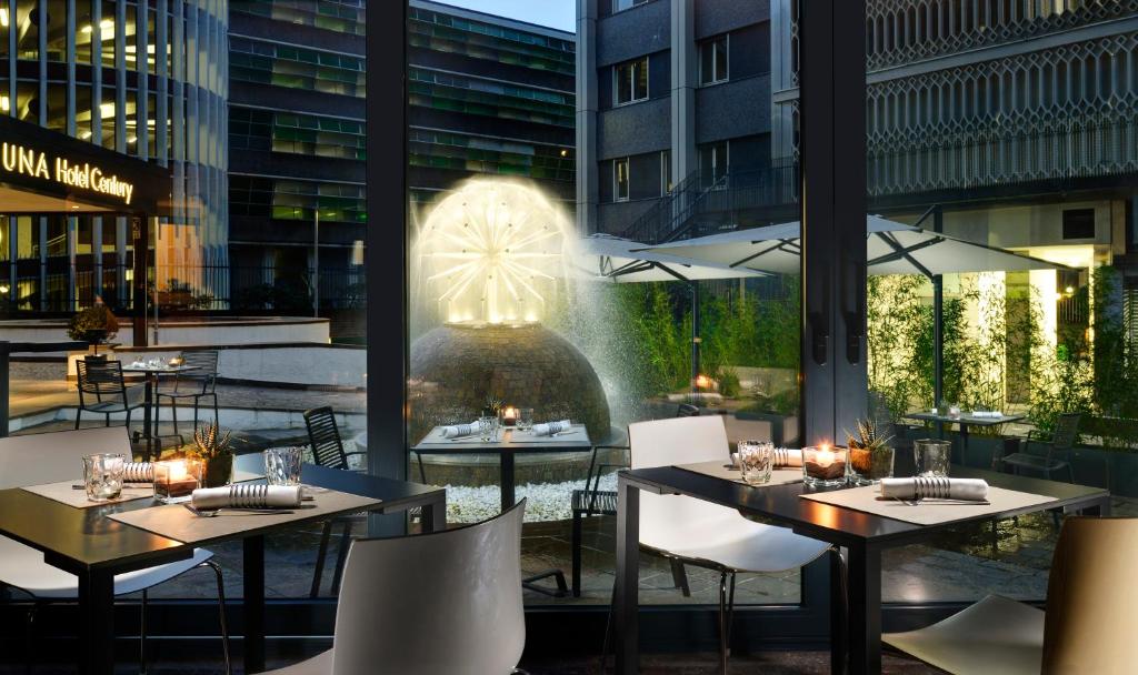 Salão para refeições do UNAHOTELS Century Milano com portas de vidro que oferecem vista para um fonte iluminada com algumas plantas ao redor, para representar hotéis perto da Estação Central em Milão
