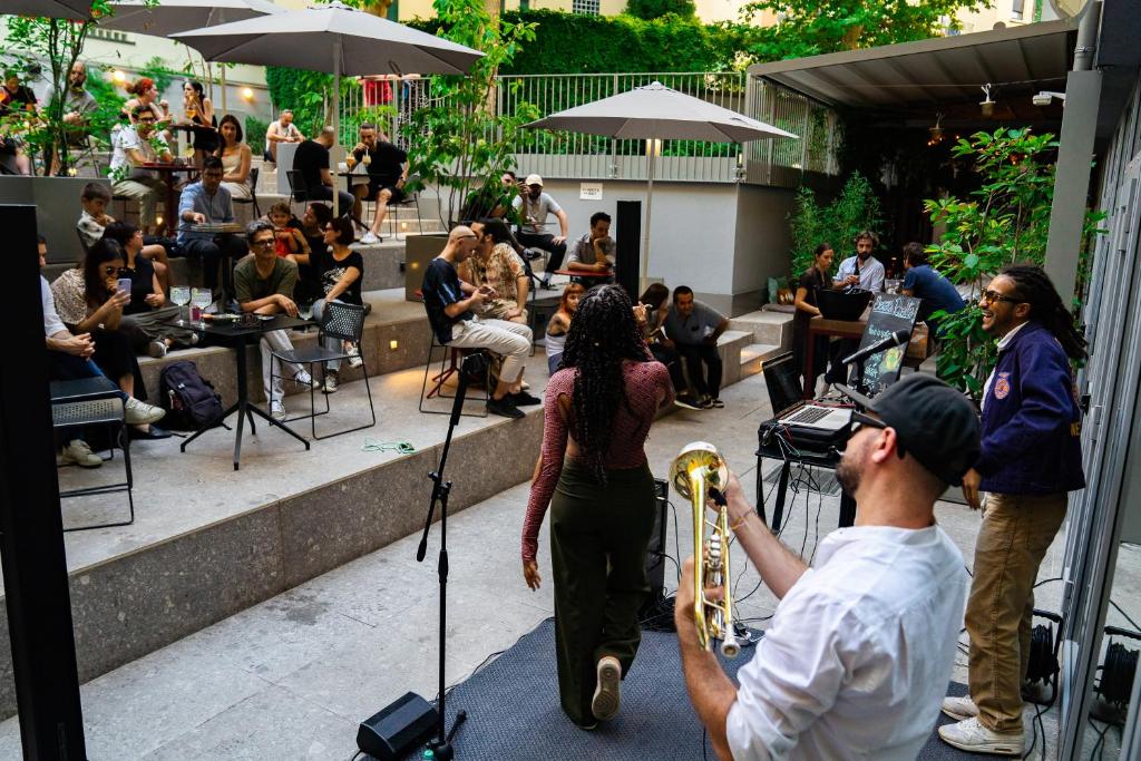 Espaço compartilhado do 21 House of Stories Città Studi com um jardim, mesas e cadeiras, há uma banda se apresentando no local
