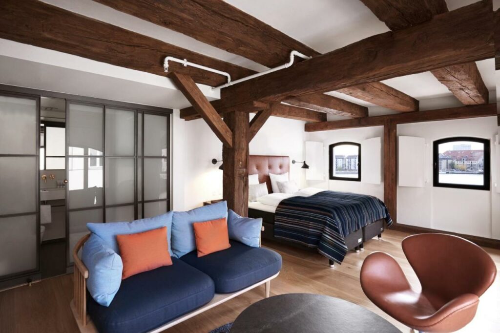 Quarto do 71 Nyhavn Hotel com duas camas formando uma cama de casal, um sofá, mesinha, cadeira e duas janelas. Foto para ilustrar post sobre hotéis em Copenhague.