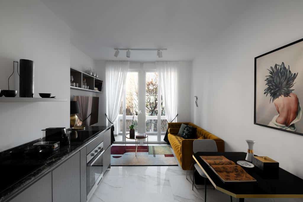 Cozinha e sala de estar do Aria Boutique Apartments Farneti, há uma sacada no local, um rack com televisão, um sofá, uma cozinha com balcão, forno e utensílios gerais, além de uma pequena mesa com duas cadeiras