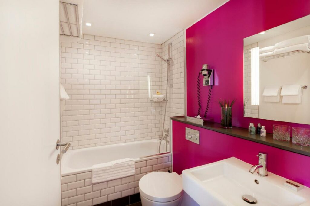 Banheiro do Andersen Boutique Hotel com uma banheira, vaso sanitário, pia, espelho e toalhas.