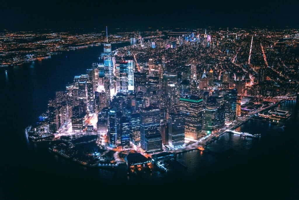 vista aérea e noturna do Financial District na Ilha de Manhattan mostrando todas as luzes acesas nos prédios e ruas da cidade.