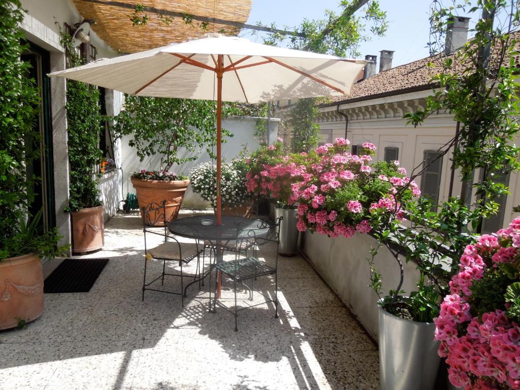 Terraço do Antica Locanda Dei Mercanti com muitos vasos de plantas e flores rosas ao redor, há uma mesinha redonda com duas cadeiras e um guarda-sol branco, para representar hotéis boutique em Milão