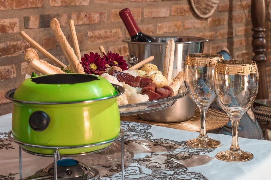 Foto de uma mesa na Pousada das Nascentes, em Brotas, com um fondue, taças, balde com champagne e uma travessa com petiscos.