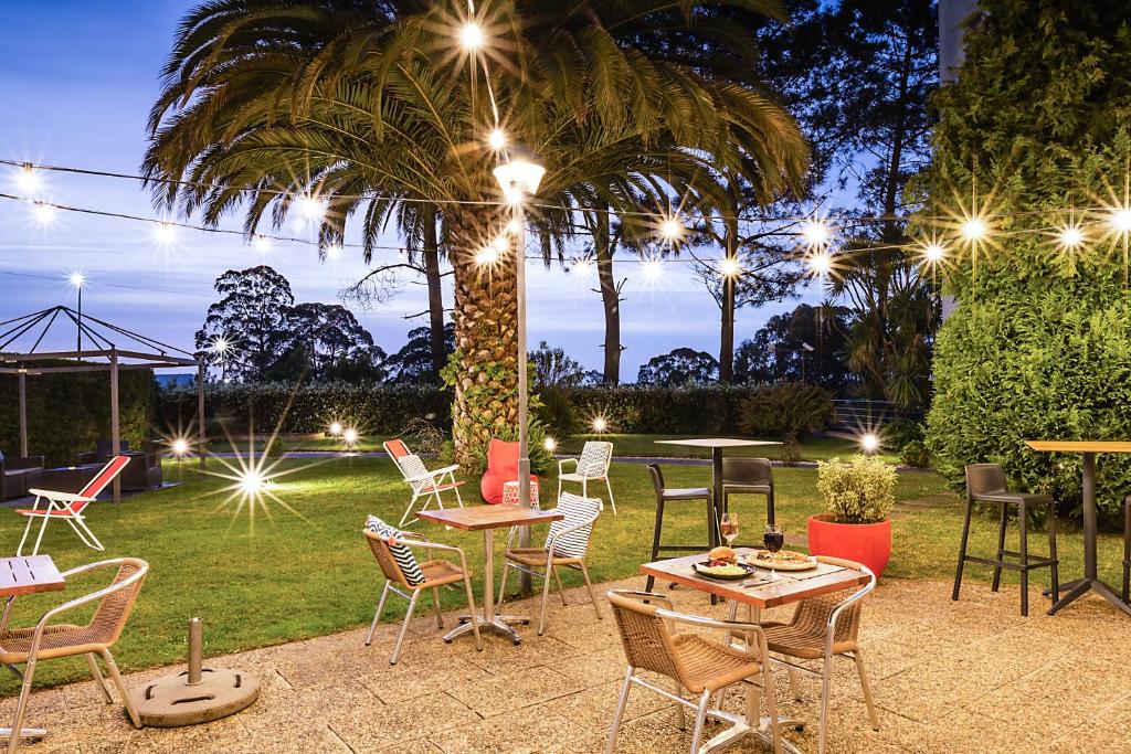 Área de estar ao ar livre no Hotel ibis Porto Gaia no final do dica com cadeiras e mesa no ambiente e árvores em volta.