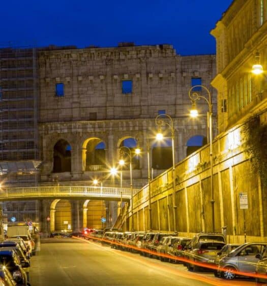 vista do Coliseu ao final da avenida em que está o Hotel Centro Cavour Roma, um dos hotéis perto do Coliseu em Roma, com carros à noite e muitas luzes