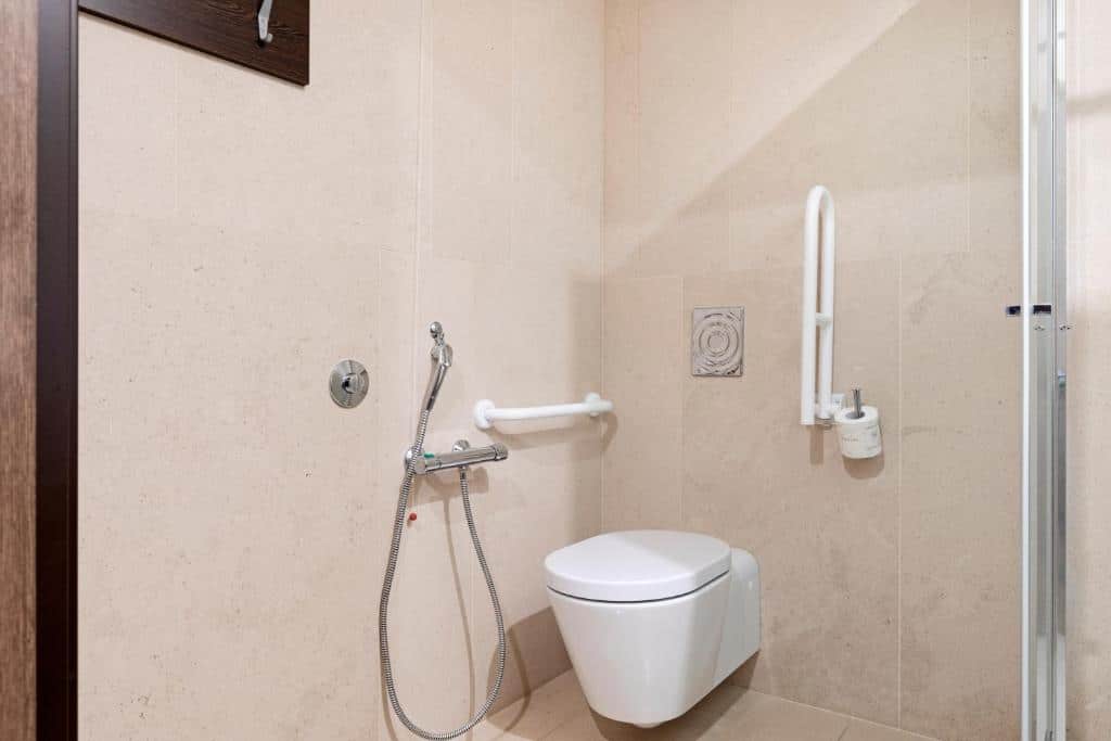 banheiro com adaptações do B&B Hotel Roma Fiumicino Aeroporto Fiera 1 como vaso sanitário mais alto, ducha higiênica e barras de apoio (em outra foto é possível ver o box aberto com cadeira de banho e mais barras de apoio)