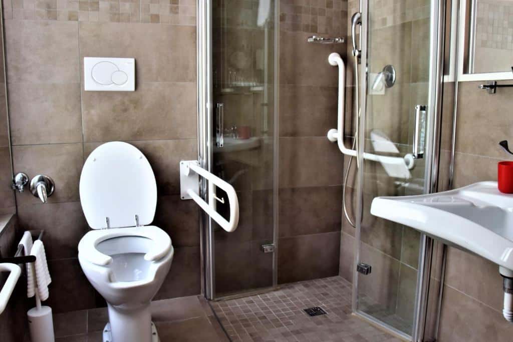 banheiro do Hotel Paolo II, um dos hotéis perto do Vaticano, com vaso sanitário adaptado, pia com espaço embaixo, barras de apoio e chuveirinho