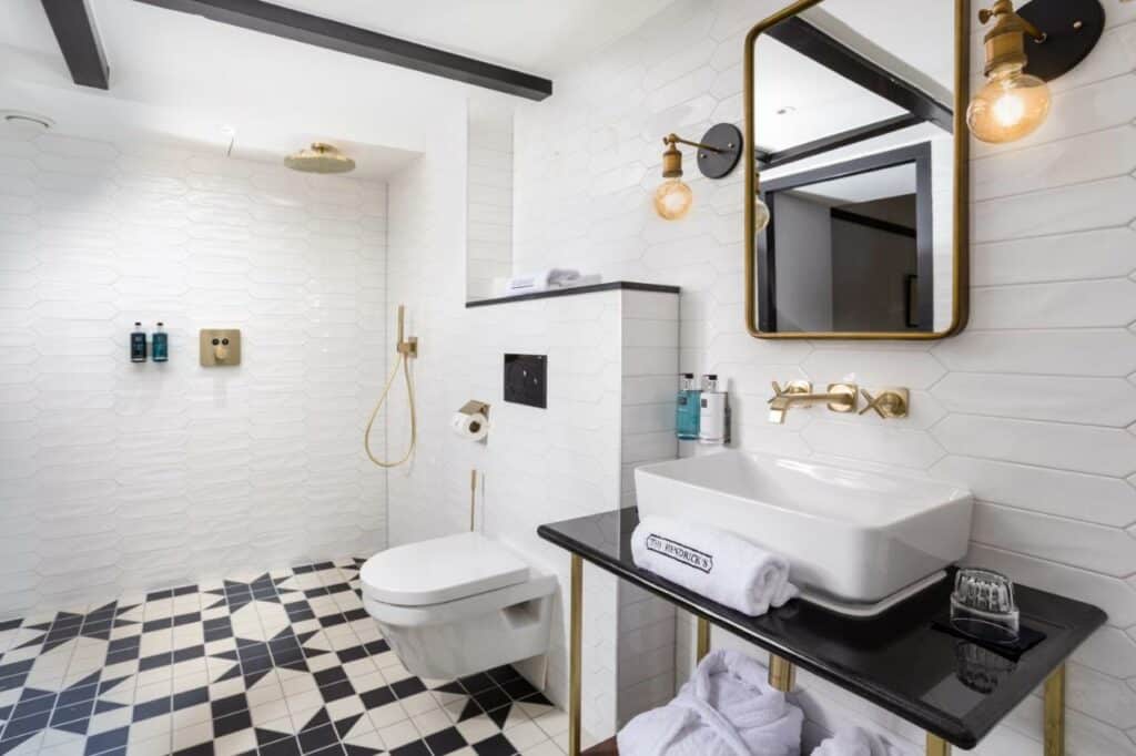 Banheiro do The Hendricks Hotel, com chão com pisos preto e branco, um móvel com pia suspensa, espelho e, ao lado, o vaso e área de banho