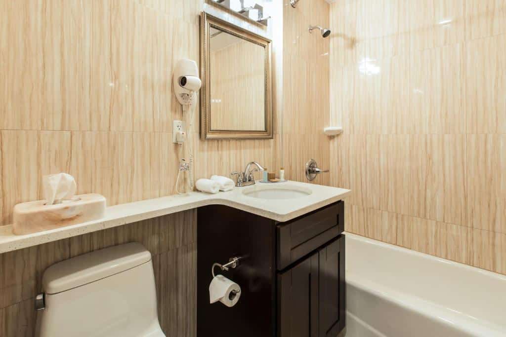 banheiro do Grandview Hotel New York com uma banheira de chão no canto direito, uma pequena cuba de pia entre a banheira e o vaso sanitário, à esquerda, e um espelho quadrado preso à parede, em cima da cuba