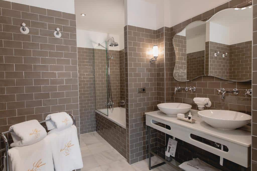 Banheiro do Hotel Gravina 51. No lado esquerdo as toalhas, no lado direito duas pias com um espelho. No fundo uma banheira com chuveiro. Foto para ilustrar post sobre Hotéis em Sevilha.