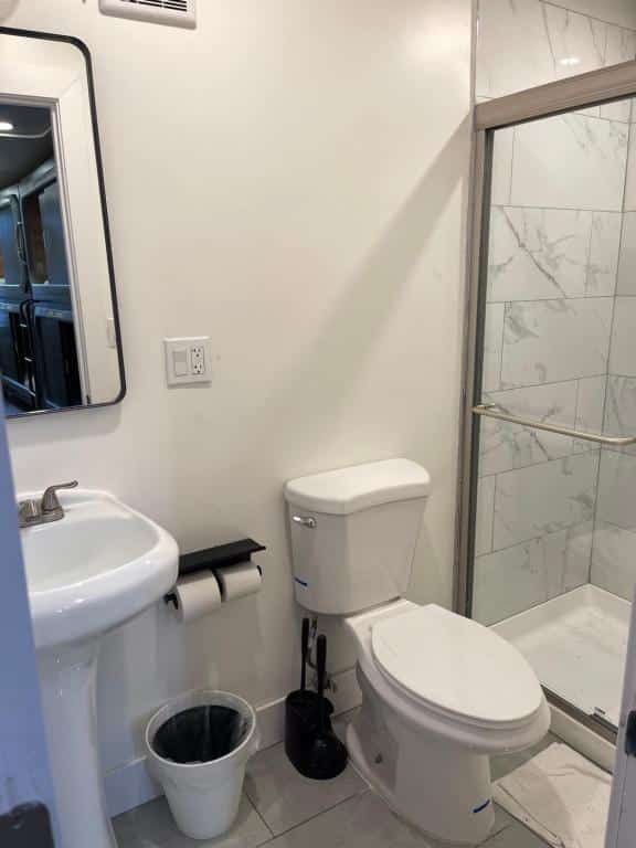 banheiro do KAMA CENTRAL PARK com uma pia de banheiro simples, um vaso sanitário e um box equipado com barras de apoio do lado de fora do chuveiro.
