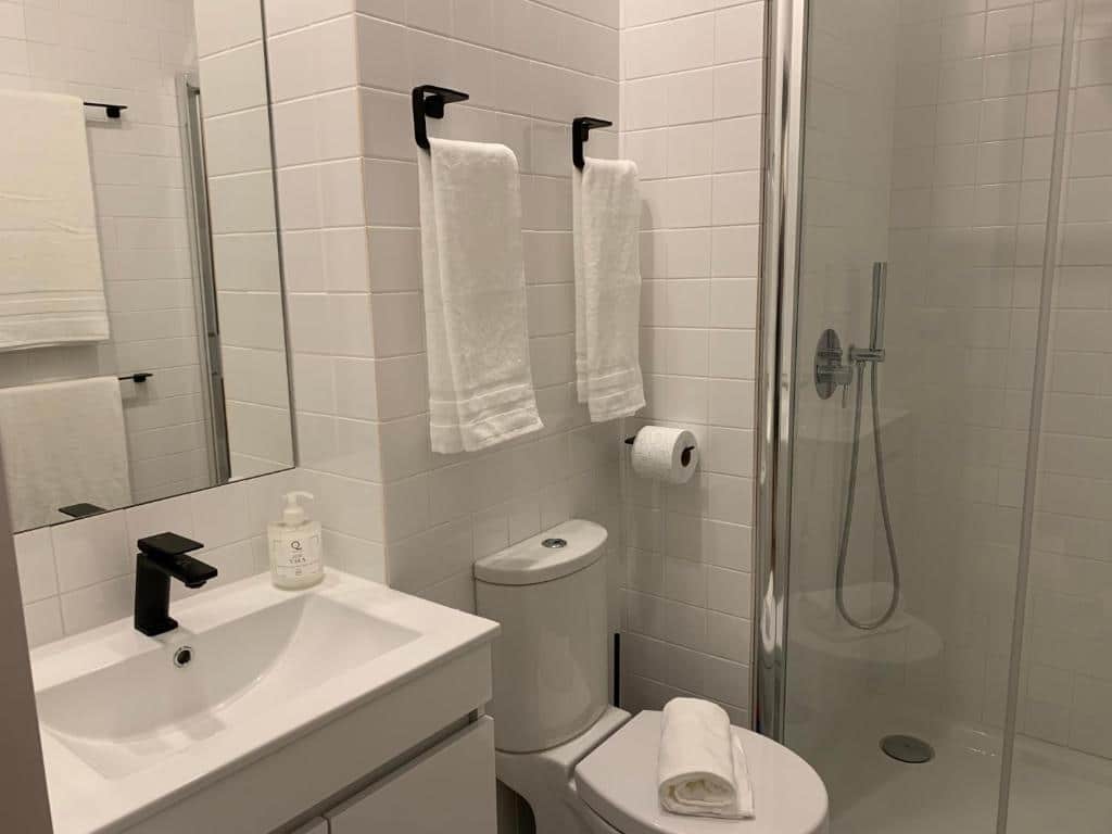 Banheiro do Lost Inn Porto Hostel com pia do lado esquerdo, vaso sanitário, box de vidro e chuveiro.