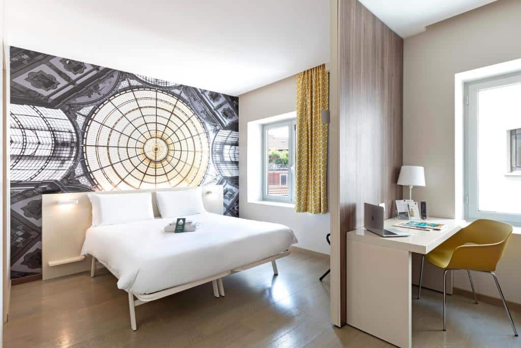 Quarto do B&B Hotel Milano Central Station com duas janelas, uma cama de casal, uma mesa de escritório com uma cadeira, para representar hotéis Mercure em Milão