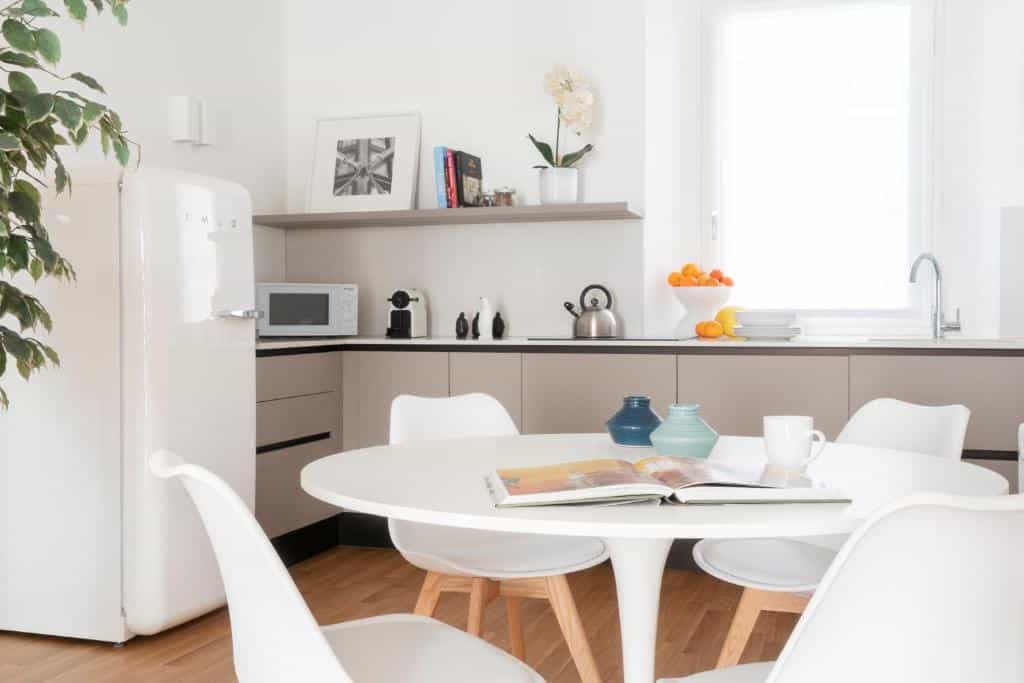 Cozinha do Brera Apartments in San Babila com uma janela com cortinas, uma geladeira, microondas, cafeteria, chaleira e itens de decoração, há também uma mesa redonda com quatro lugares, para representar airbnb em Milão