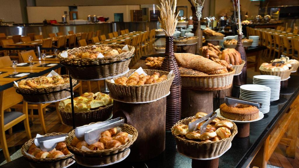Buffet de café da manhã do Holiday Inn Parque Anhembi. A foto foi tirada no restaurante, e em cima da mesa do buffet vemos os alimentos dentro de cestas, como pães, doces e bolos.
