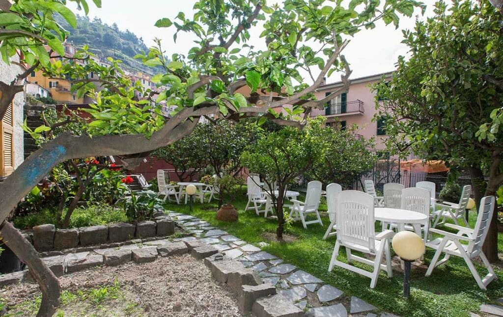 Parte do hotel com várias árvores verdes, jardim e gramado com mesas e cadeiras brancas durante o dia, ilustrando post Hotéis em Cinque Terre.