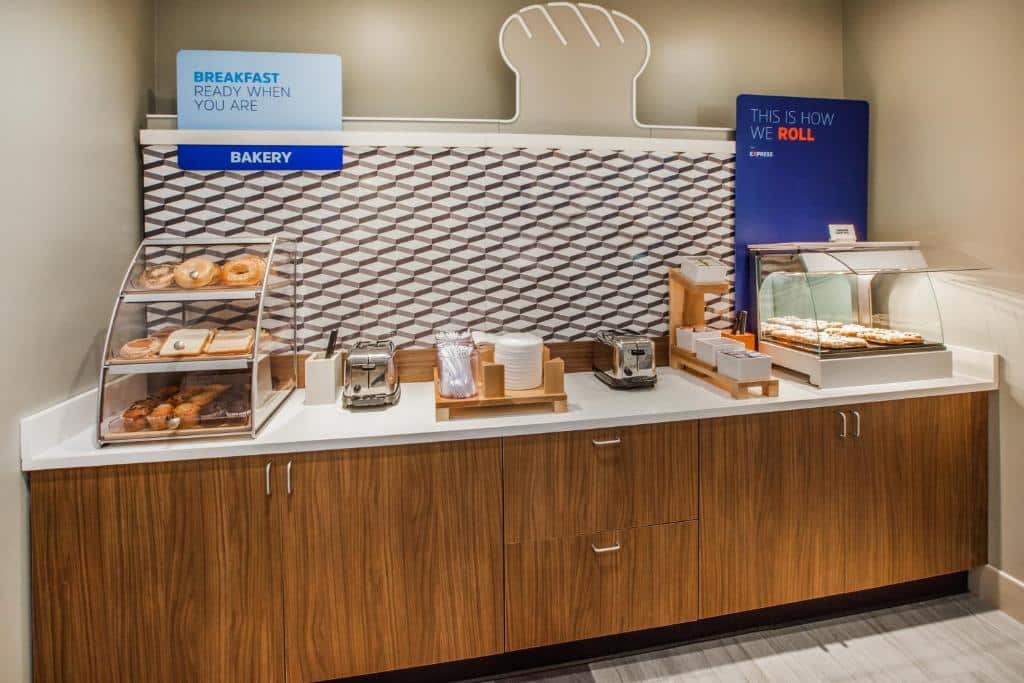 área de café da manhã do Holiday Inn Express com diferentes pães, donuts, bages e cinnamon rolls dispostos para comer.