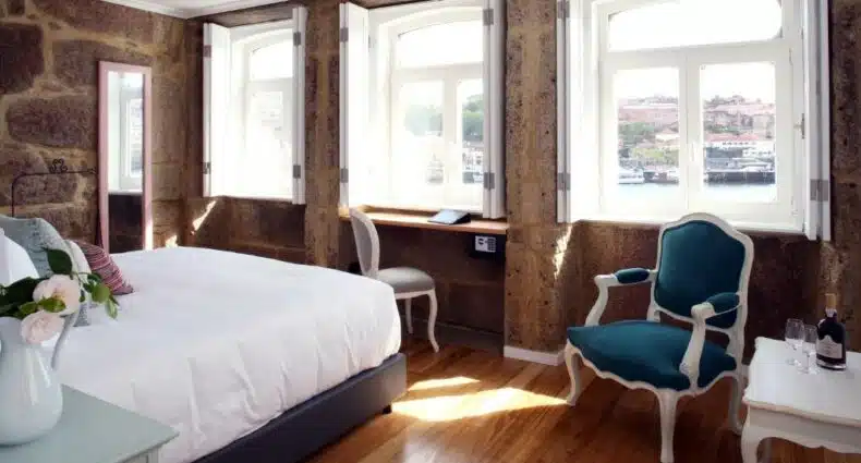 Quarto do 1872 River House com cama grande do lado esquerdo e uma poltrona do lado direito, e três janelas grandes deixando o quarto bem iluminado. Representa hotéis boutique no Porto.
