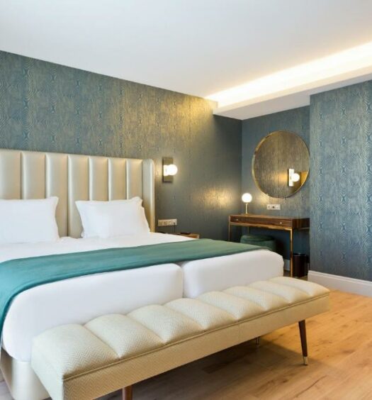 Quarto do Acta The Avenue com cama de casal do lado esquerdo com um banco estofado ao pé da cama. Representa hotéis baratos no Porto.