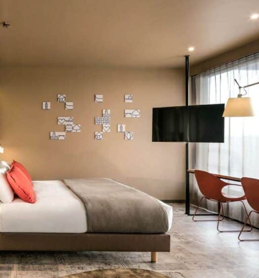 Quarto do Mercure Porto Centro Santa Catarina com cama de casal do lado esquerdo da imagem, em frente a cama umamesa com duas cadeiras e do lado esquerdo da cama em frente uma TV. Representa hotéis Mercure no Porto.