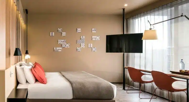 Quarto do Mercure Porto Centro Santa Catarina com cama de casal do lado esquerdo da imagem, em frente a cama umamesa com duas cadeiras e do lado esquerdo da cama em frente uma TV. Representa hotéis Mercure no Porto.