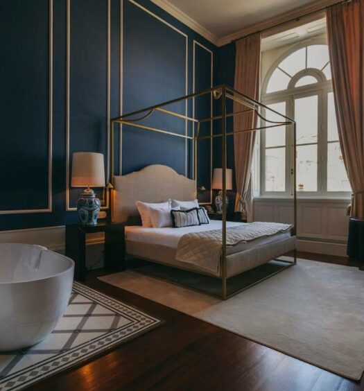 Quarto amplo do Torel 1884 Suites & Apartments com cama de casal do lado esquerdo com duas comodas ao lado da cama com luminária, ainda do lado esquerdo uma banheira redonda. Representa hotéis românticos no Porto.