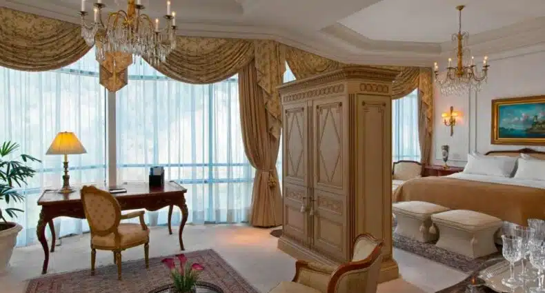 Quarto amplo do Sheraton Santiago Hotel & Convention Center com cama do lado direito, em frente a cama uma cômoda de madeira e uma área de estar do lado esquerdo. Representa hotéis em Providencia em Santiago.