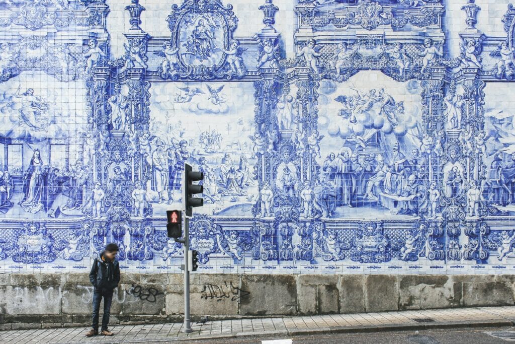 Imagem da faixada da Capelas das Almas no Porto com um homem parado do lado do semáforo durante o dia.