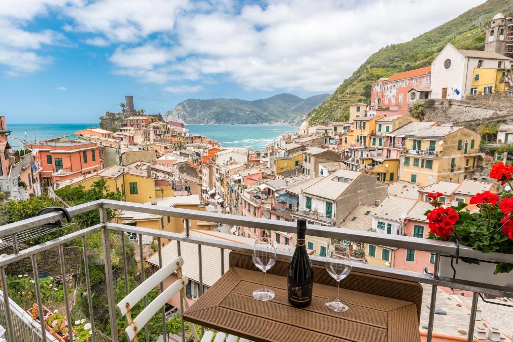 Mesa marrom com duas taças e uma garrafa de champanhe na sacada aberta com vista para as construções coloridas da cidade, montanhas e o mar azul no fundo, ilustrando post Hotéis em Cinque Terre.