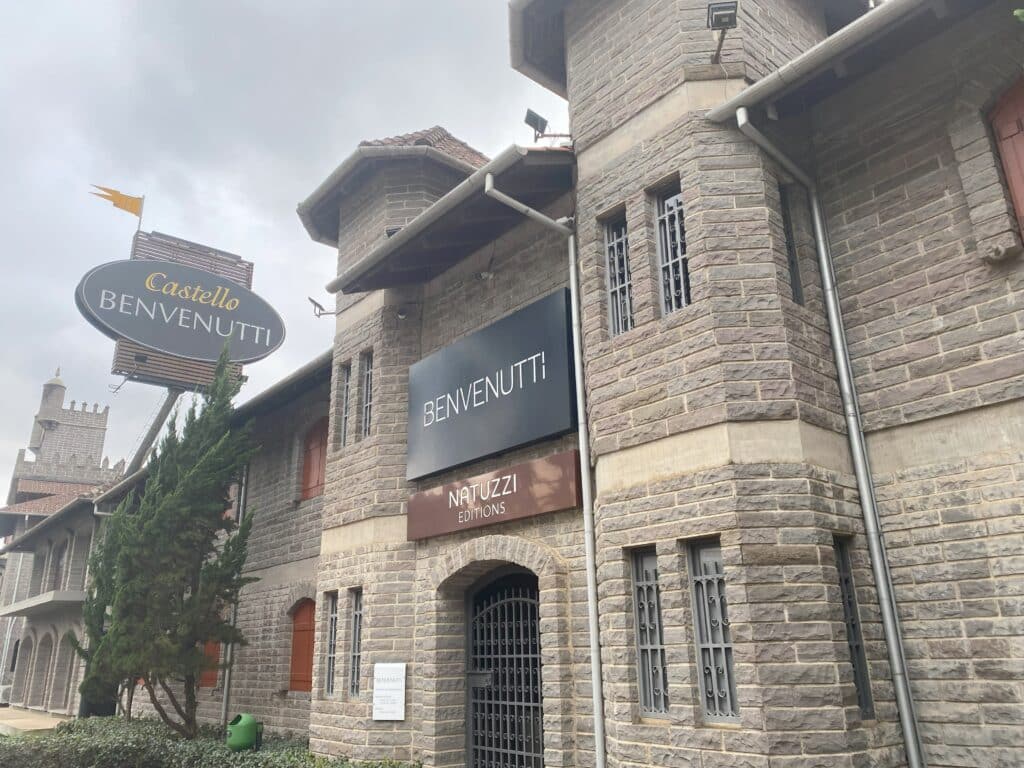 A fachada externa do Castello Benvenutti, com paredes de tijolinhos e janelinhas estreitas, além de grade em casa uma delas e também na porta