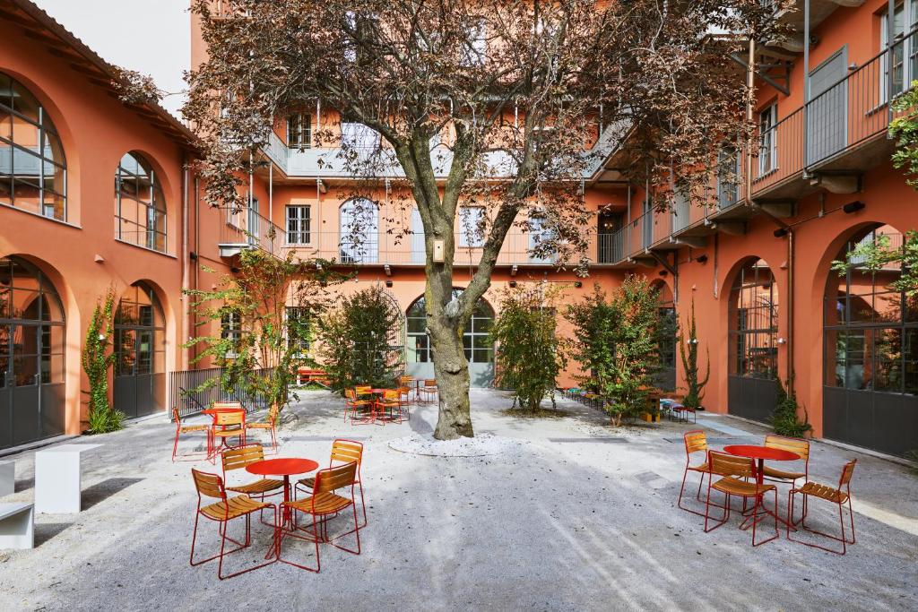 Pátio aberto do Combo Milano com uma árvore grande no centro, e alguns arbustos ao redor, há mesas e cadeiras para sentar-se no local