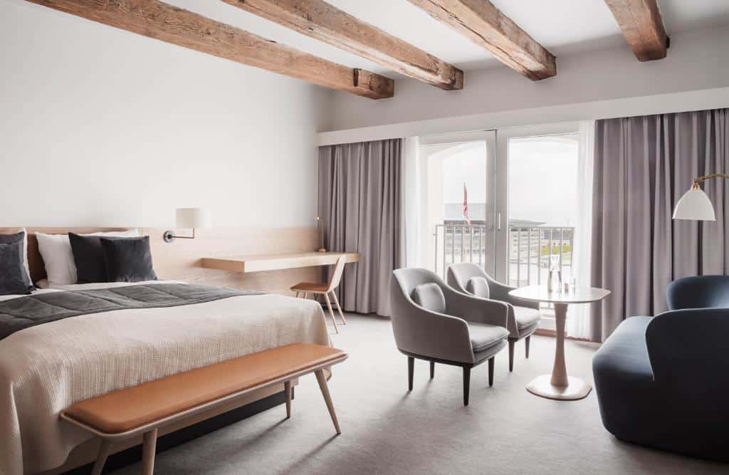 Quarto do Copenhagen Admiral Hotel com uma cama de casal, poltronas, duas mesas, cadeira e um recamier ao pé da cama. Há também uma varanda. Foto para ilustrar post sobre hotéis em Copenhague.