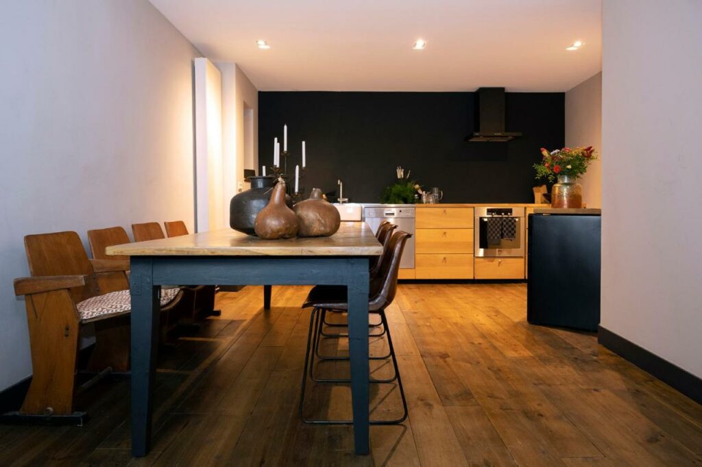 Cozinha do St Antonis Apartment, com uma mesa retangular com 6 cadeiras e a cozinha ao fundo. A cozinha tem um balcão de madeira com pia, forno e lava-louças embutidos e a parede atrás é preta
