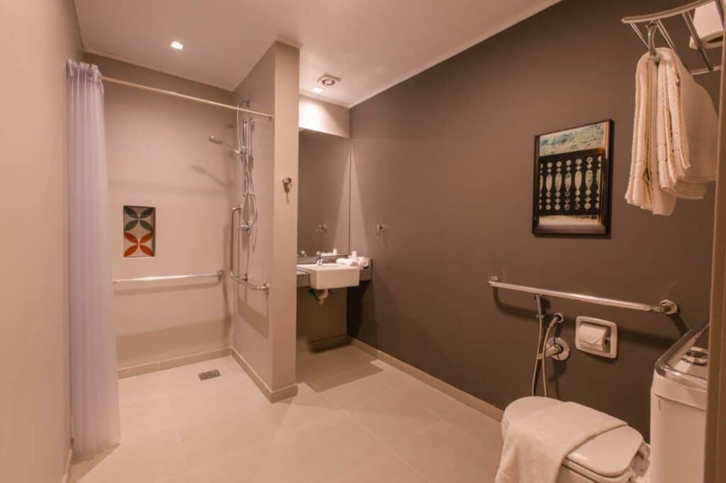 Banheiro amplo e adaptado para pessoas com deficiência no Dall'Onder Ski Hotel, com barras de apoio, pia rebaixada e vaso sanitário elevado
