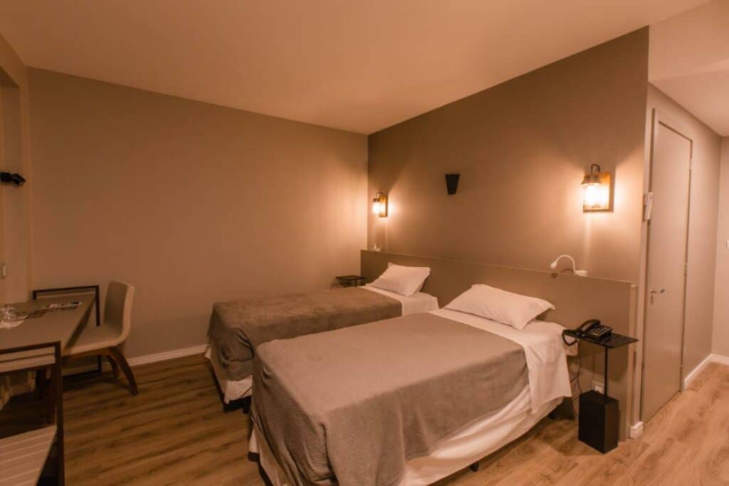 Quarto com duas camas de solteiro, uma mesa de trabalho com cadeira, iluminação amarelada e mesinha de cabeceira com telefone, no Dall'Onder Ski Hotel