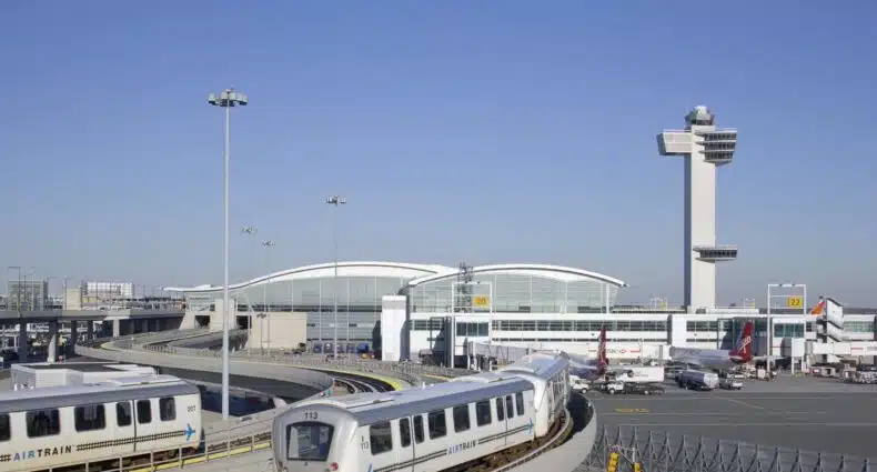 vista da área externa do aeroporto internacional JFK de Nova York mostrando duas trilhas com carros de metrô à esquerda da imagem e à direita, alguns aviões taxiando na pista de pouso, para representar hotéis perto do Aeroporto JFK em Nova York