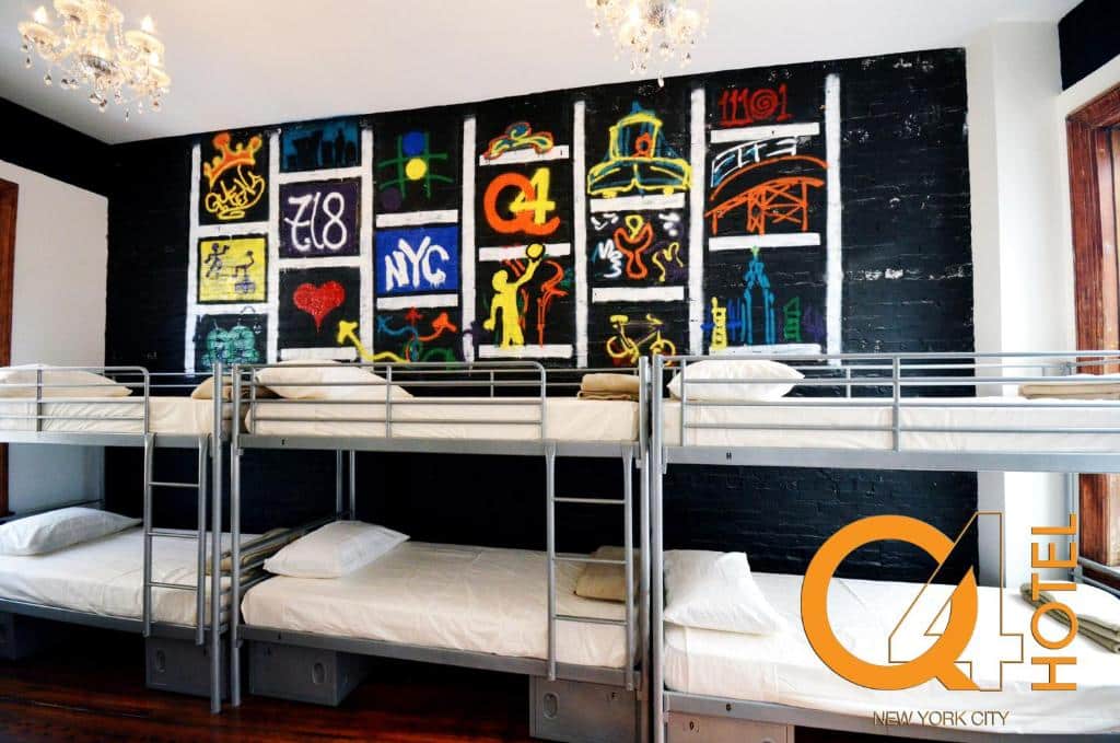 dormitório do Q4 Hotel and Hostel em Nova York com três beliches, lado a lado, encostadas à parede do fundo do quarto, que está toda pintada de preto e com alguns desenho pichados.