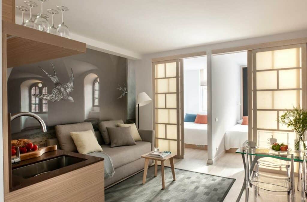 Apartamento Clique na imagem e faça sua reserva em Eric Vökel Boutique Apartments - Copenhagen Suites. Há um sofá, uma pia de cozinha, mesa de refeições e dois quartos ao fundo.