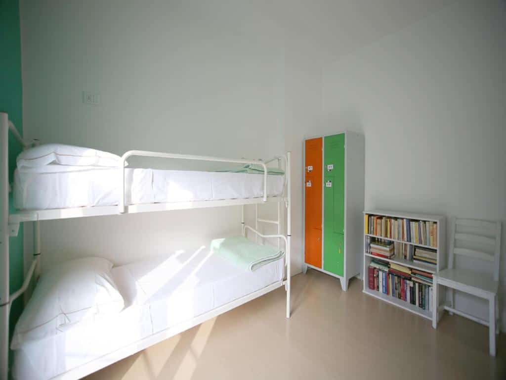 Quarto do Gogol'Ostello & Caffè Letterario com uma beliche branca com almofadas, um armário com chave em verde e laranja, além de um móvel com diversos livros disponíveis