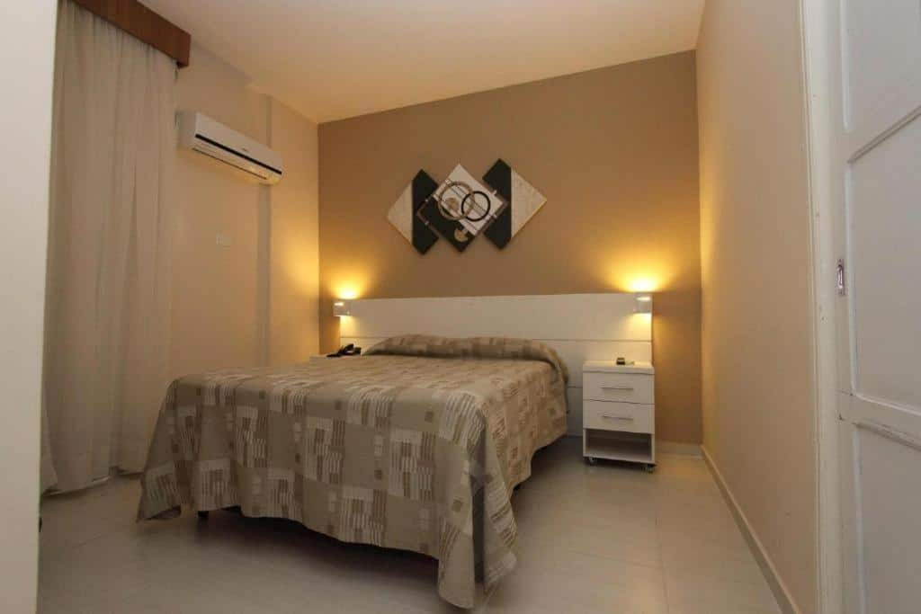 Quarto do Gonzaga Flat com uma cama de casal, mesinha de cabeceira, ar-condicionado e luminárias.