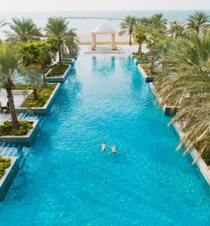 Uma ampla piscina do Hilton Ras Al Khaimah Beach Resort de frente para praia, com muitas palmeiras ao redor, para representar hotéis de luxo em Ras Al Khaimah