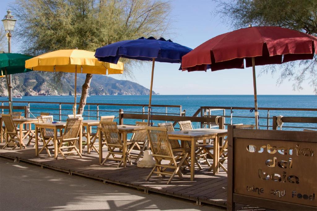 Uma placa com o nome do hotel, várias mesas e cadeiras de madeira com guarda-sóis em frente ao mar durante o dia, ilustrando post Hotéis em Cinque Terre.
